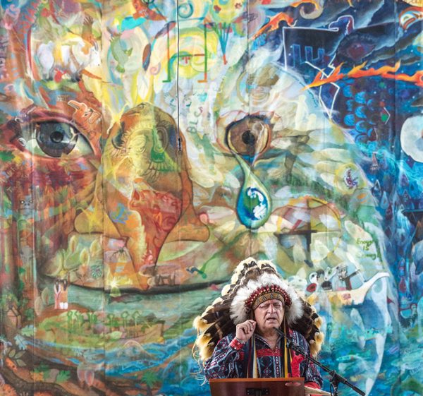 Chief Phil Lane Jr. speaking at a podium in front of the travelling mural, hung as the backdrop at St Mark&rsquo;s Episcopal Cathedral in Seattle